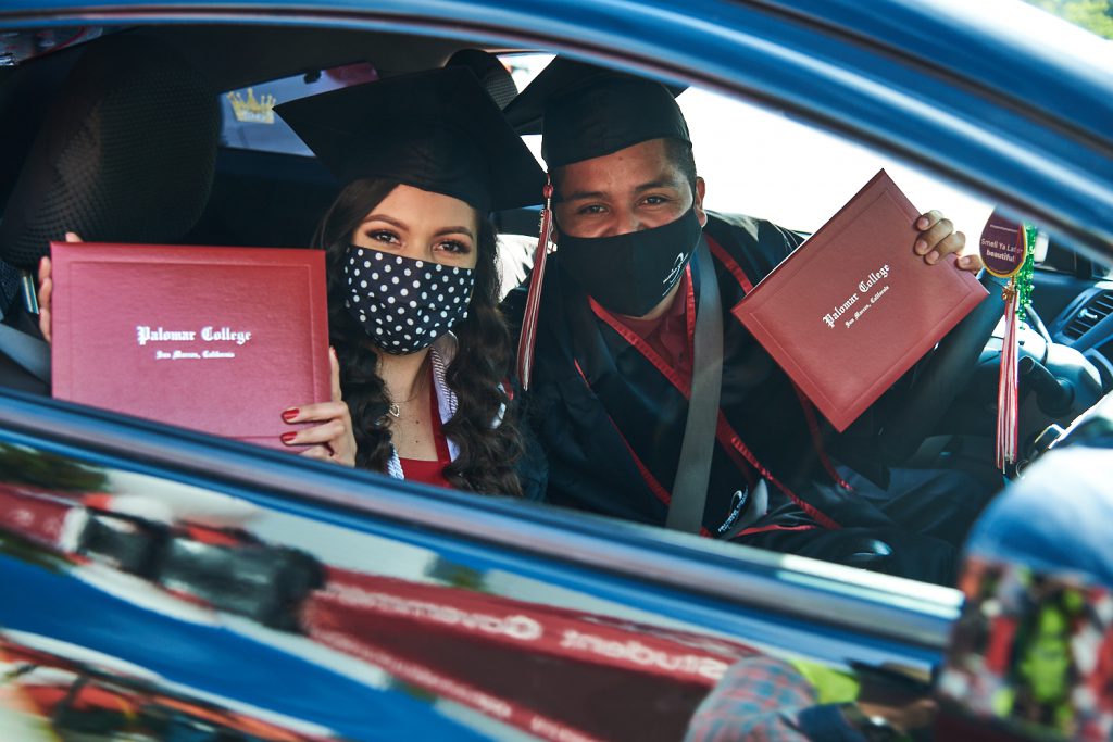 Students holding diplomas in their car at the drive through commencement ceremony