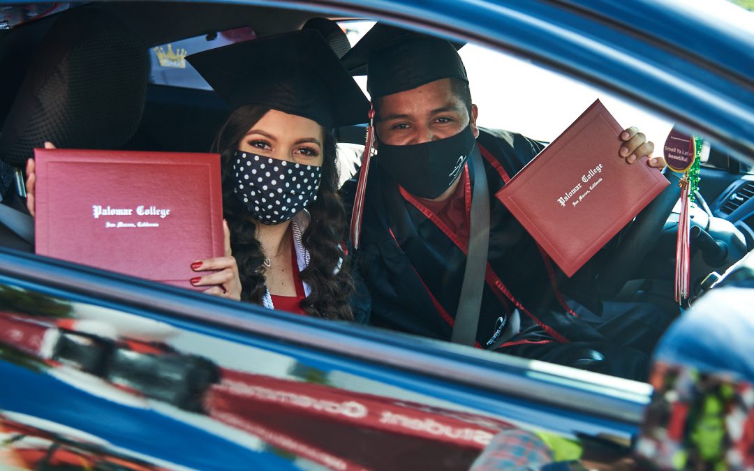 Students holding diplomas in their car at the drive through commencement ceremony