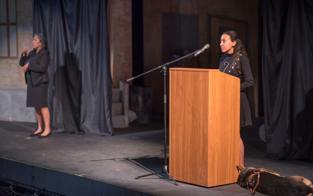 Haben Girma stands at a podium on stage at Palomar College's Brubeck Theatre, while her sign language interpreter stands to the left