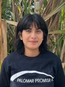 Linsay is in a black Palomar Promise shirt smiling in front of the school's sugar cane.