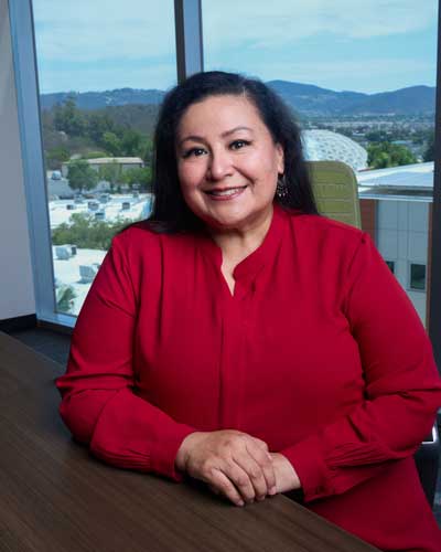 Dr. Star Rivera-Lacey Ph.D. wearing a red blouse, smiling, and seated at a conference table.