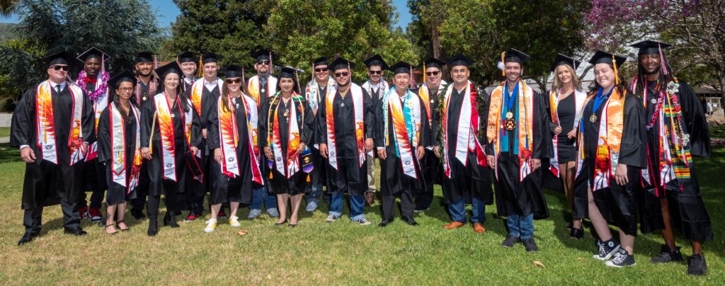 The photo shows a group of students wearing caps and gowns for graduation.