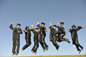 Photo of group of college graduates jumping in the air on a hill top 