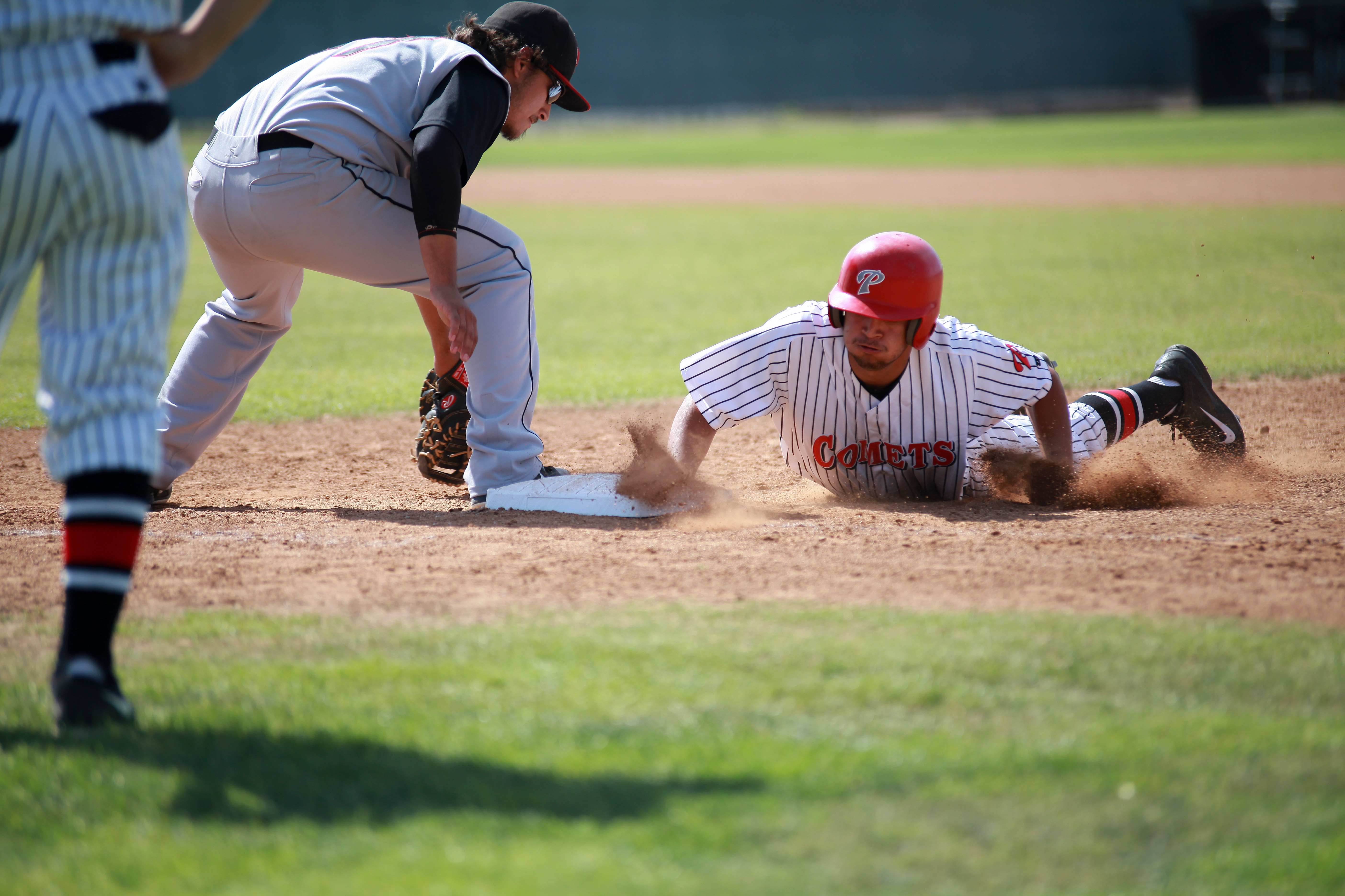 A Palomar baseball player slides to a base on his stomach as an opposing player crouches above him with his mitted hand near the ground.