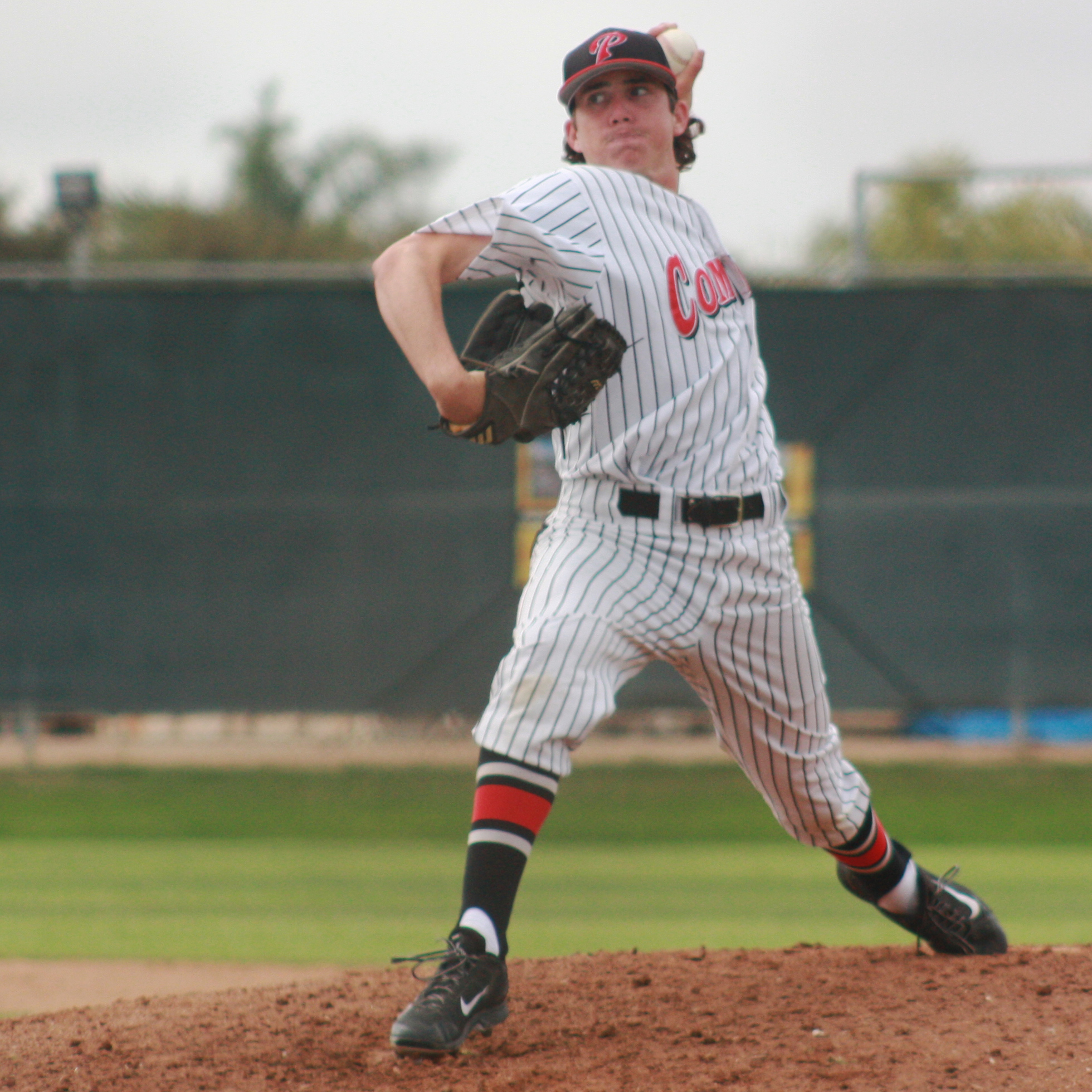 A male Palomar baseball player prepares to throw a baseball with his left hand, his left leg and foot extended behind him.
