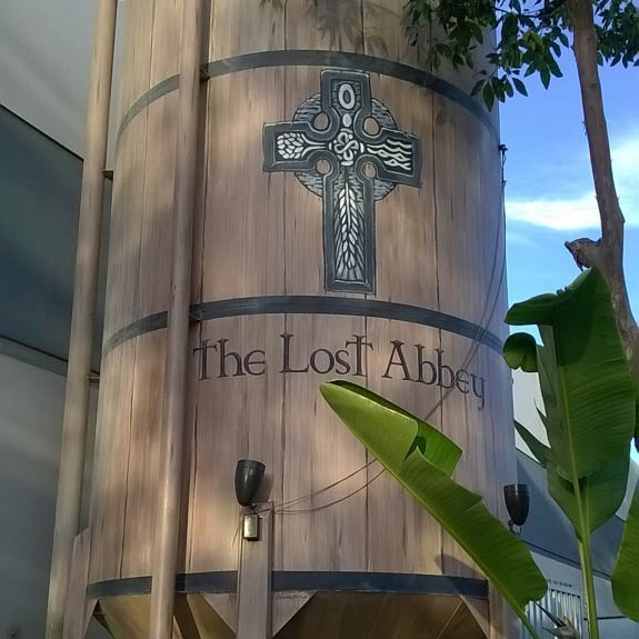 A 25-foot beer fermenter stands at the entrance of The Lost Abbey brewery in San Marcos. Engraved on the fermenter is a crucifix which pictures the four elements necessary to create beer. On the four flanks of the cross, above is a seed of yeast, on the left are hops, while the right flank depicts waves of water, and the bottom flank shows grain. (Steven Buriek/ The Telescope)