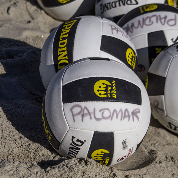 Several white and black volleyballs lie in the sand with the word "PALOMAR" written on it in faded black ink.