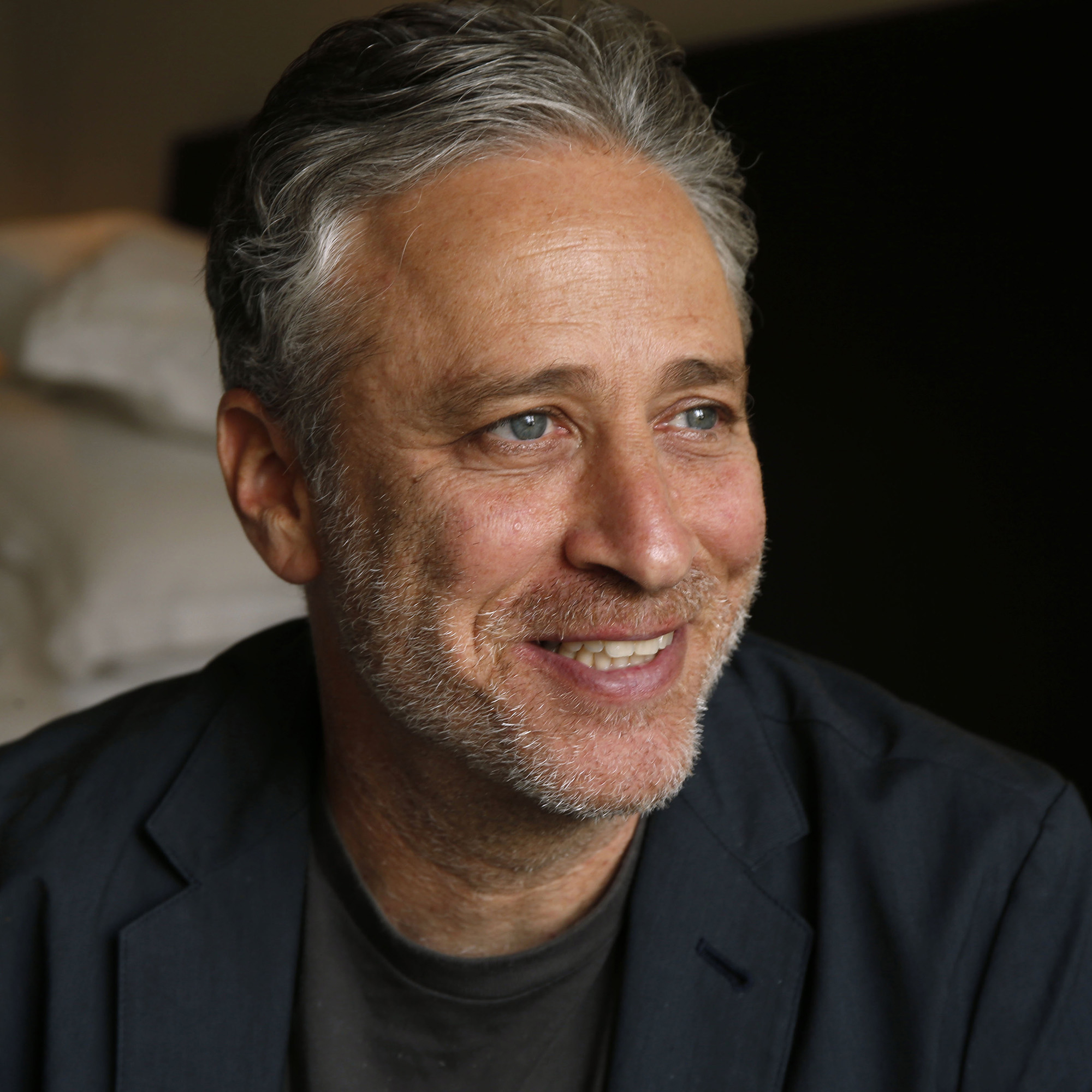 Writer-director Jon Stewart sits and smiles, facing slightly to the right.