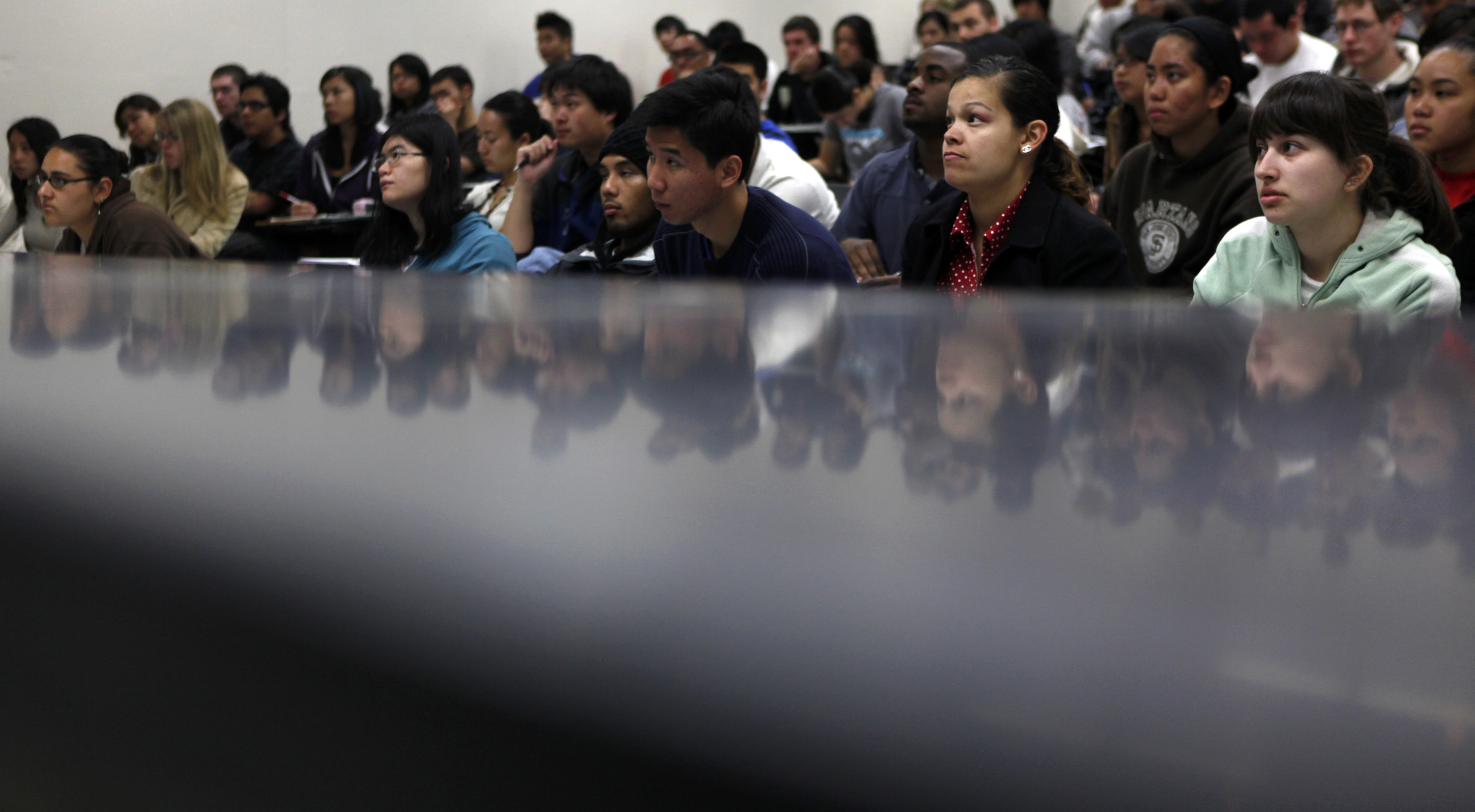 Many students sit and listen to a lecture in a lecture hall.