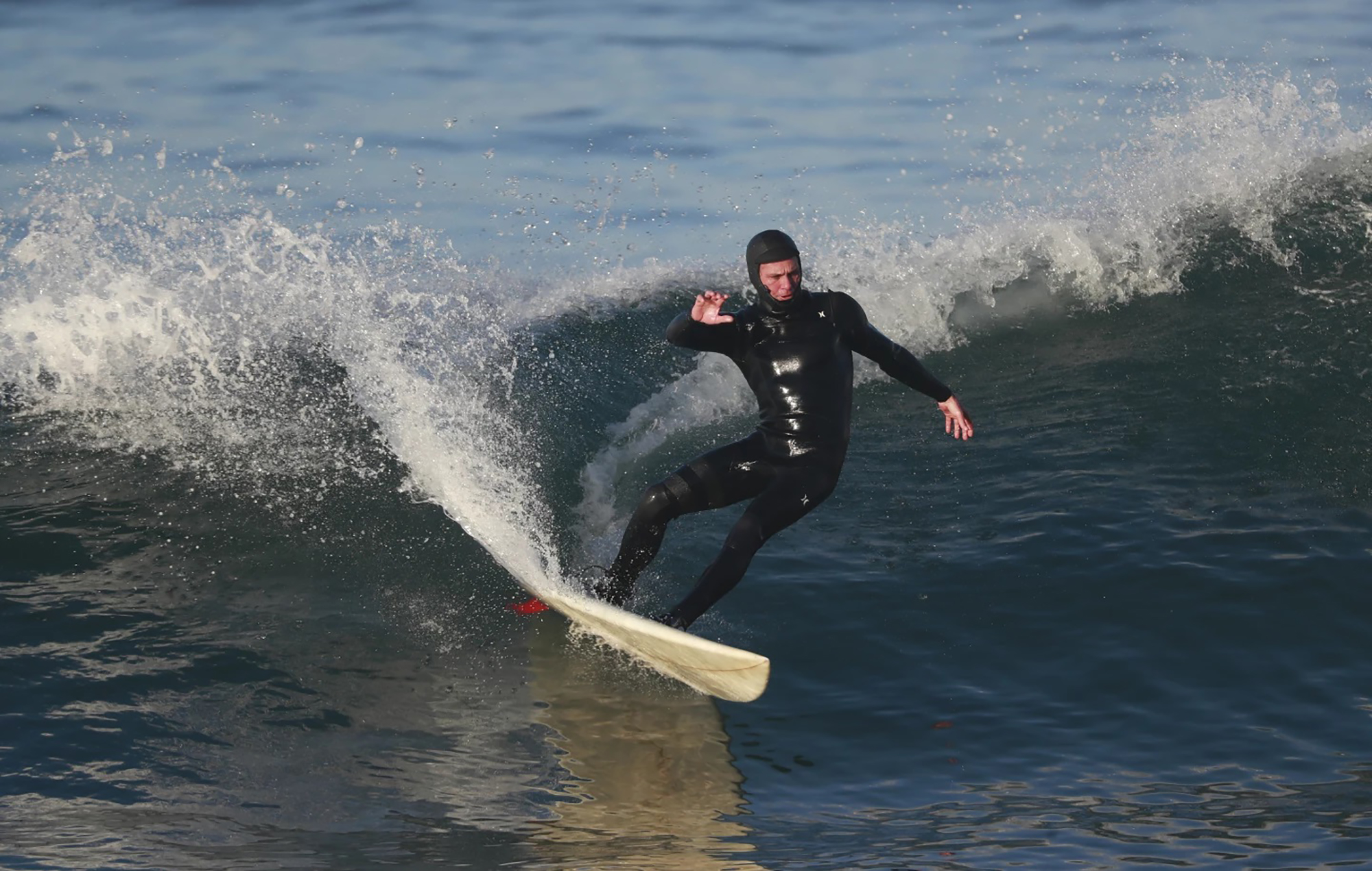 A man wearing a black wet suit surfs on a white surfboard.