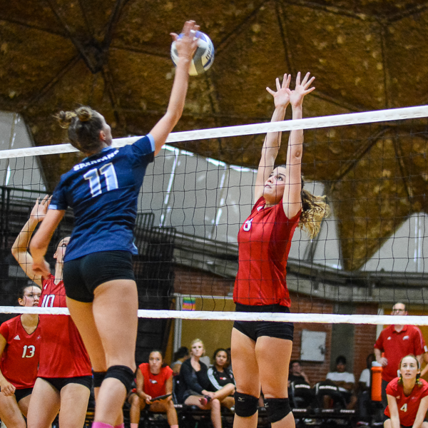 A female Palomar volleyball player tries to block the ball from going over the net after the opponent spikes it.