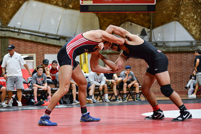 Two male wrestlers grapple each other while their foreheads touch. They both wear earguards.