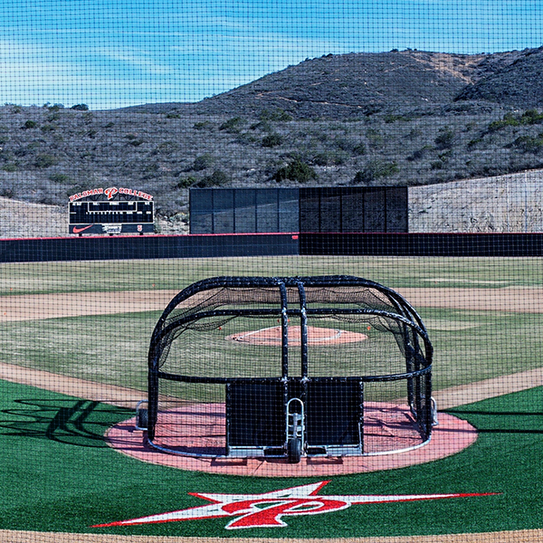 Palomar College's new baseball field with the battle cage in the foreground and a scoreboard in the background. Hills covered with dry brush are in the background.
