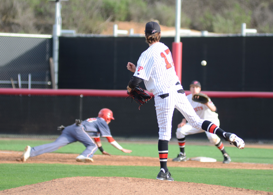 A male Palomar baseball player throws a baseball to another player who is about to catch it as an opposing player dives to the ground to slide to base.
