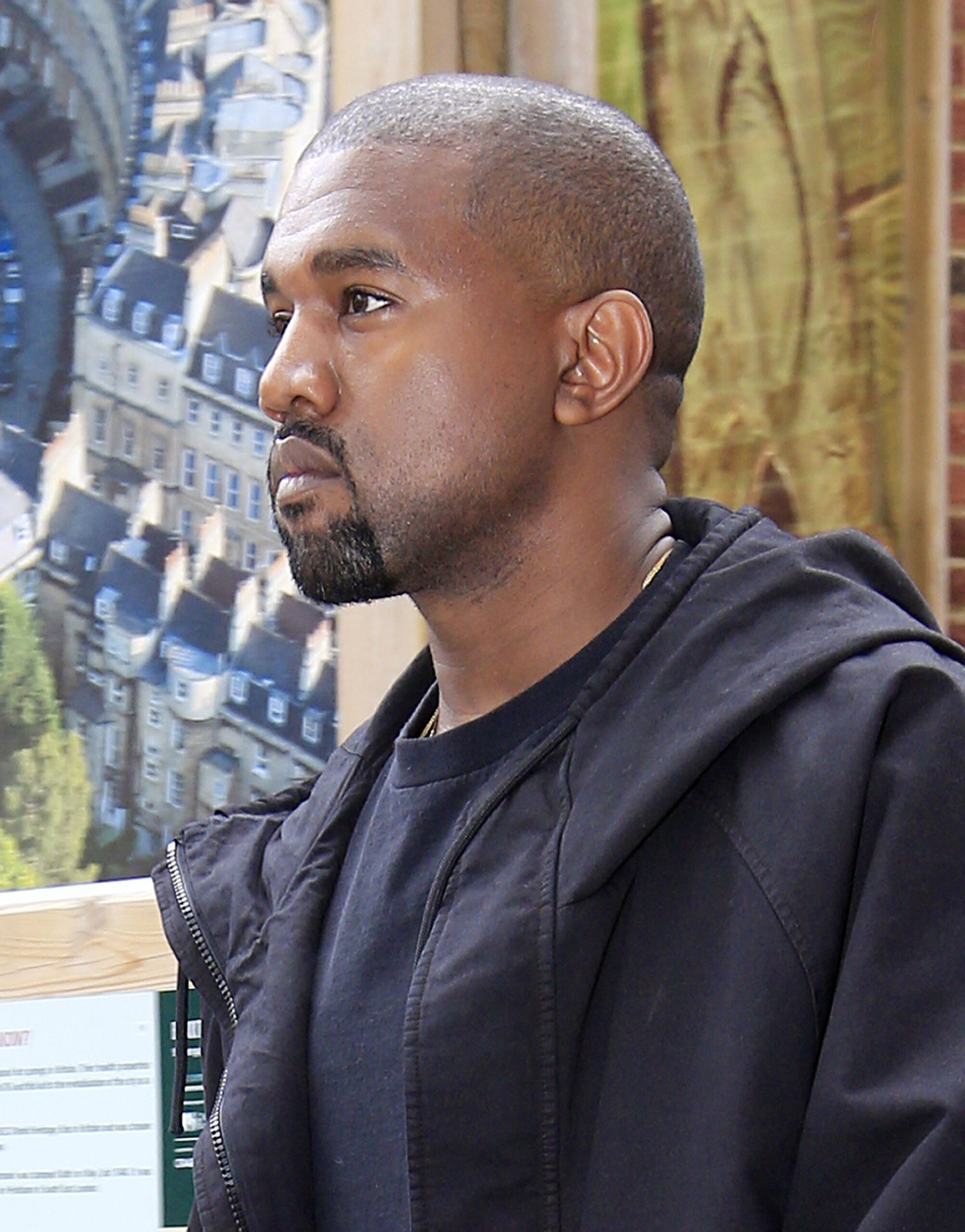 Kanye West wears a dark blue jacket and T-shirt, looking ahead.