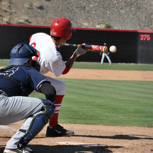 A male Palomar baseball player bunts a baseball while a catcher in a blue jersey and helmet watches from behind in a squat position.