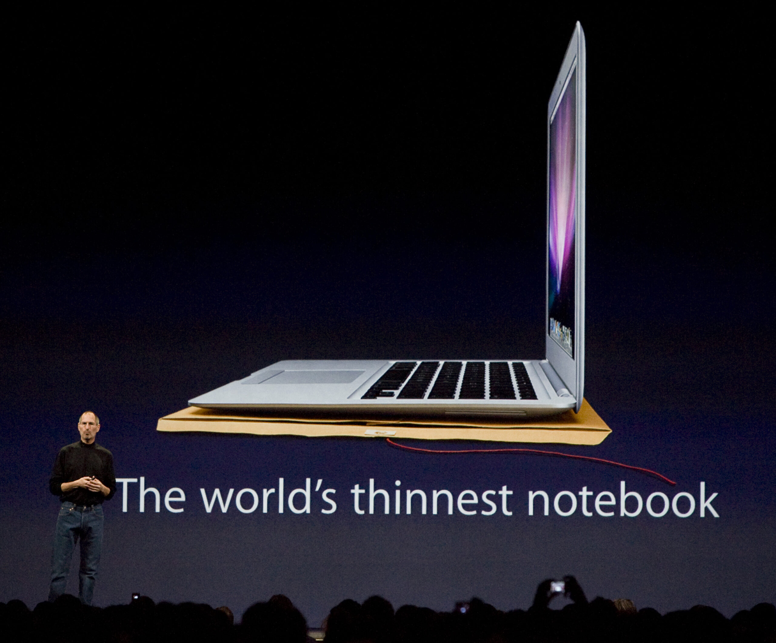 Apple CEO Steve Jobs stands in front of a screen with a picture of an Apple Macbook laptop with the text "The world's thinnest notebook" below it.