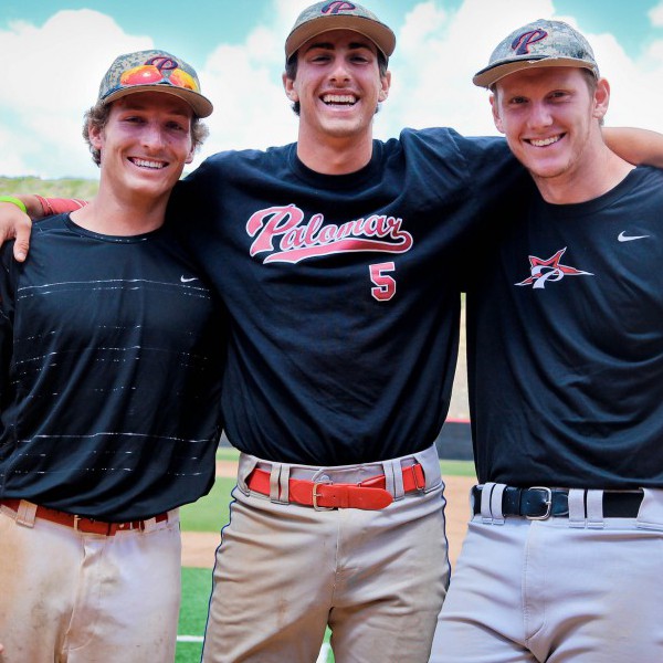 Three Palomar baseball players smile for a picture with their arms around each others' shoulders. They're wearing black T-shirts and white pants.