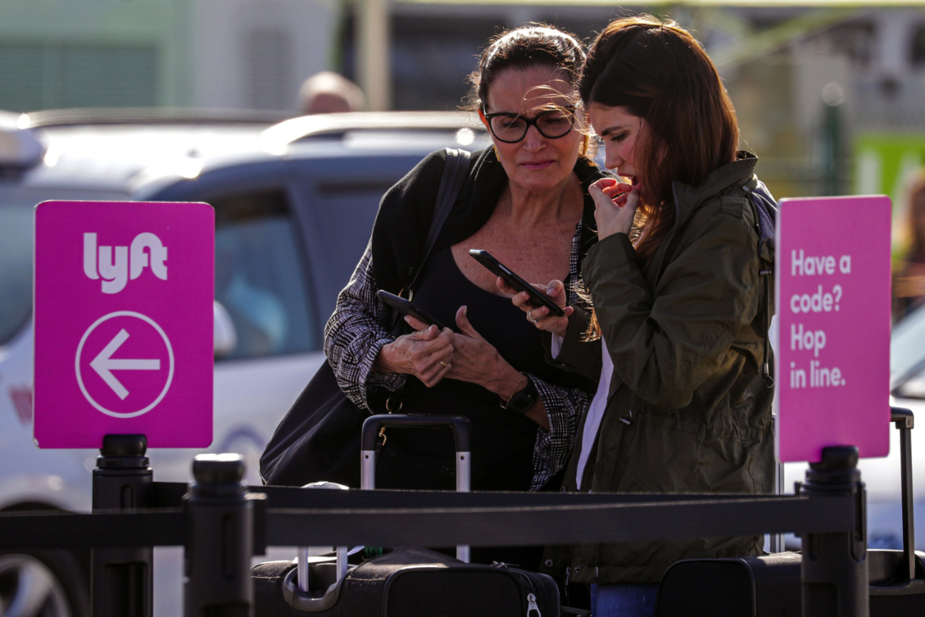 Two women check their smartphone for a Lyft ride at an airport.