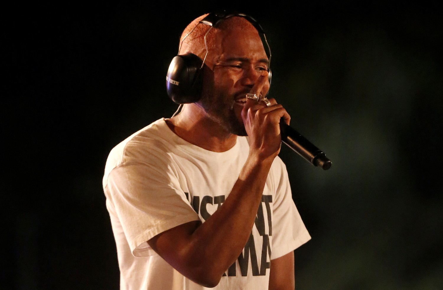 Frank Ocean sings while holding a microphone to his mouth and wearing headphones.