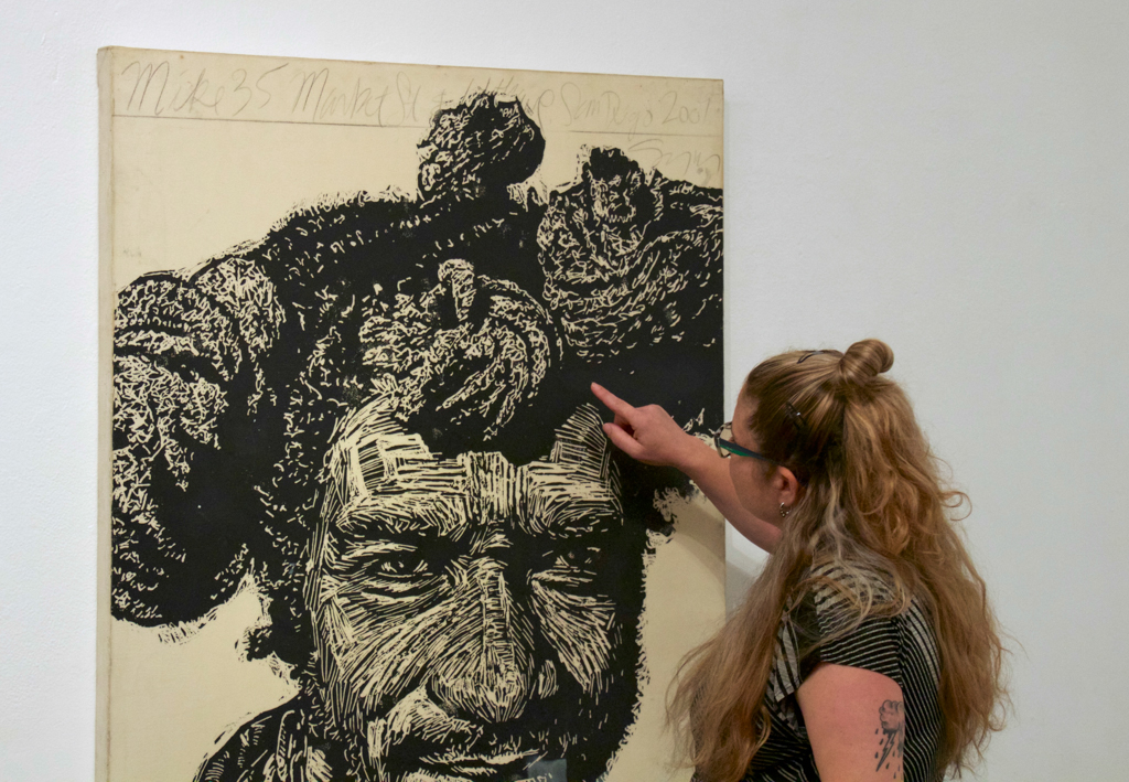 Gallery Director Sasha Reibstein pints out the detail in a portrait by artist Neil Shigley for the Boehm Gallery's exhibition "We The People" at Palomar College. (Michael Schulte/The Telescope)