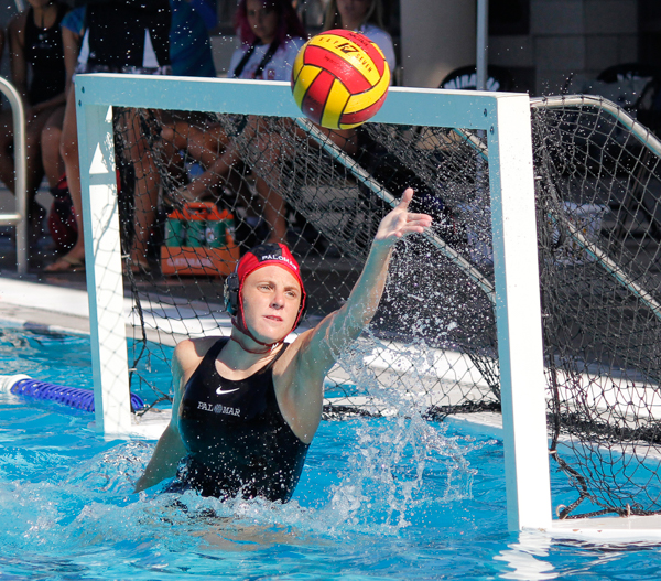 A male Palomar water polo player tries to block a ball from going into the goal with his left hand.