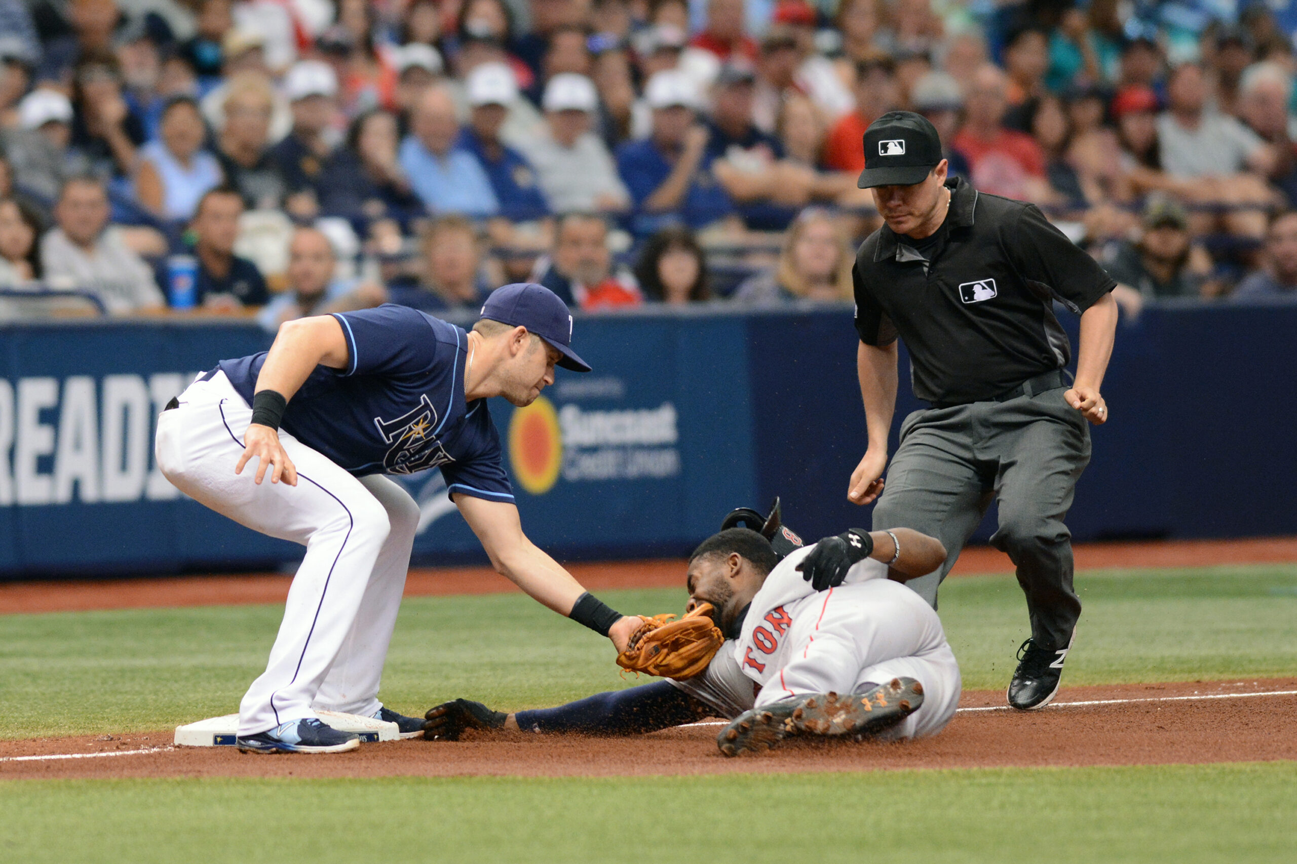 A baseball player slides to a base as a baseman tags him with a baseball in his mitt. An umpire follows the slider behind him.