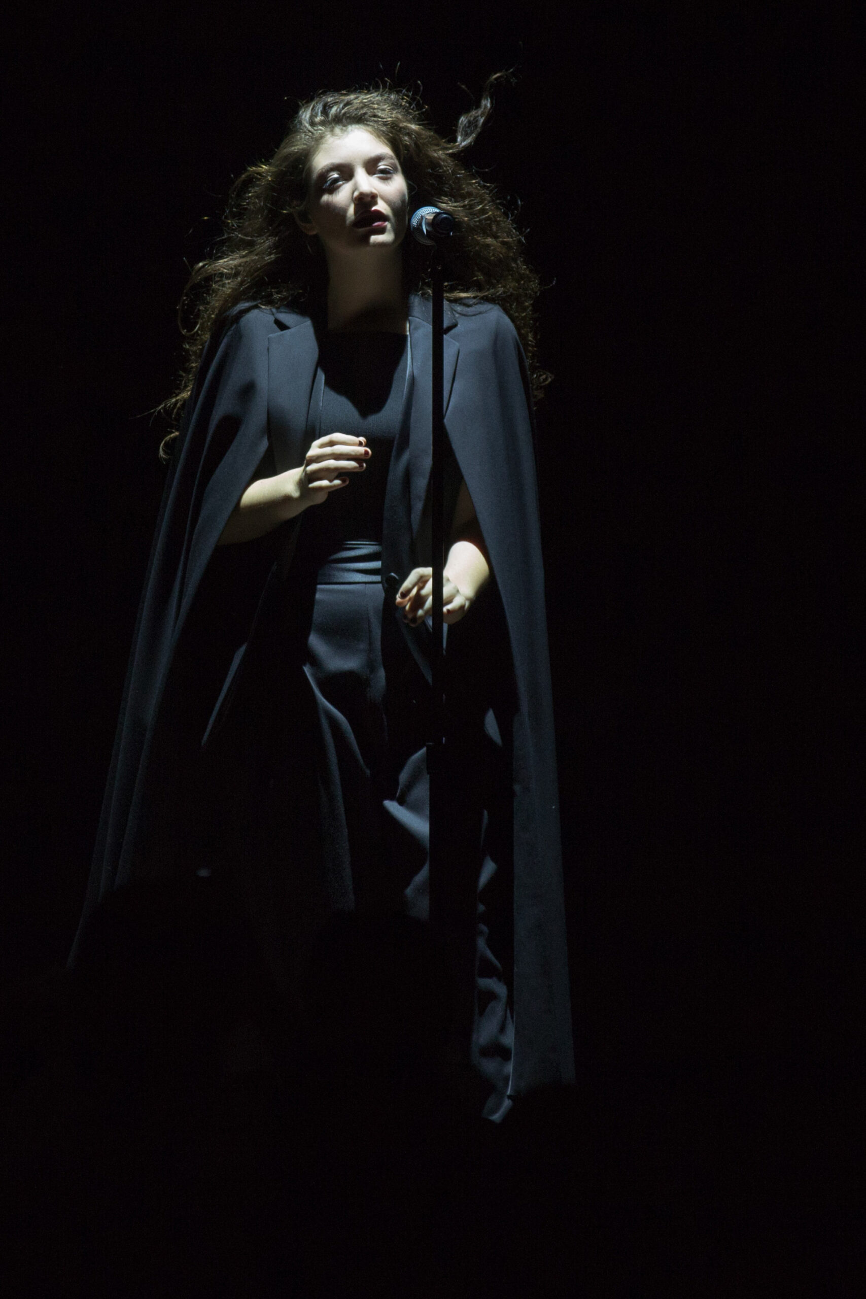 Singer Lorde sings and wears a black cloak and black "suit" with a single spotlight shining on her face.