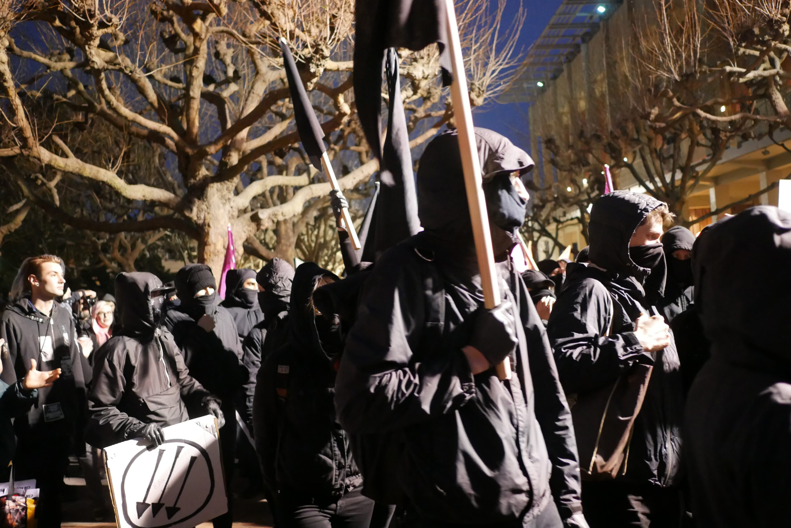 A group of protesters were hooded jackets and cloth masks, carrying a black flag.