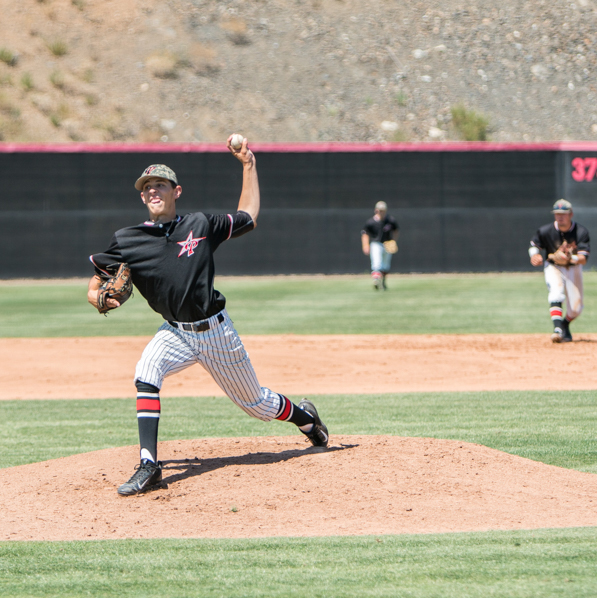 A male Palomar baseball pitcher throws a baseball with his left hand, his right leg steps in front of him. Two of his teammates are in the background in the outfield.