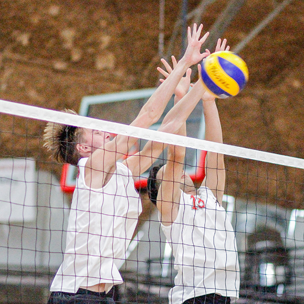 Two male Palomar volleyball players block a ball from going over the net as an opponent on the right spikes the ball.