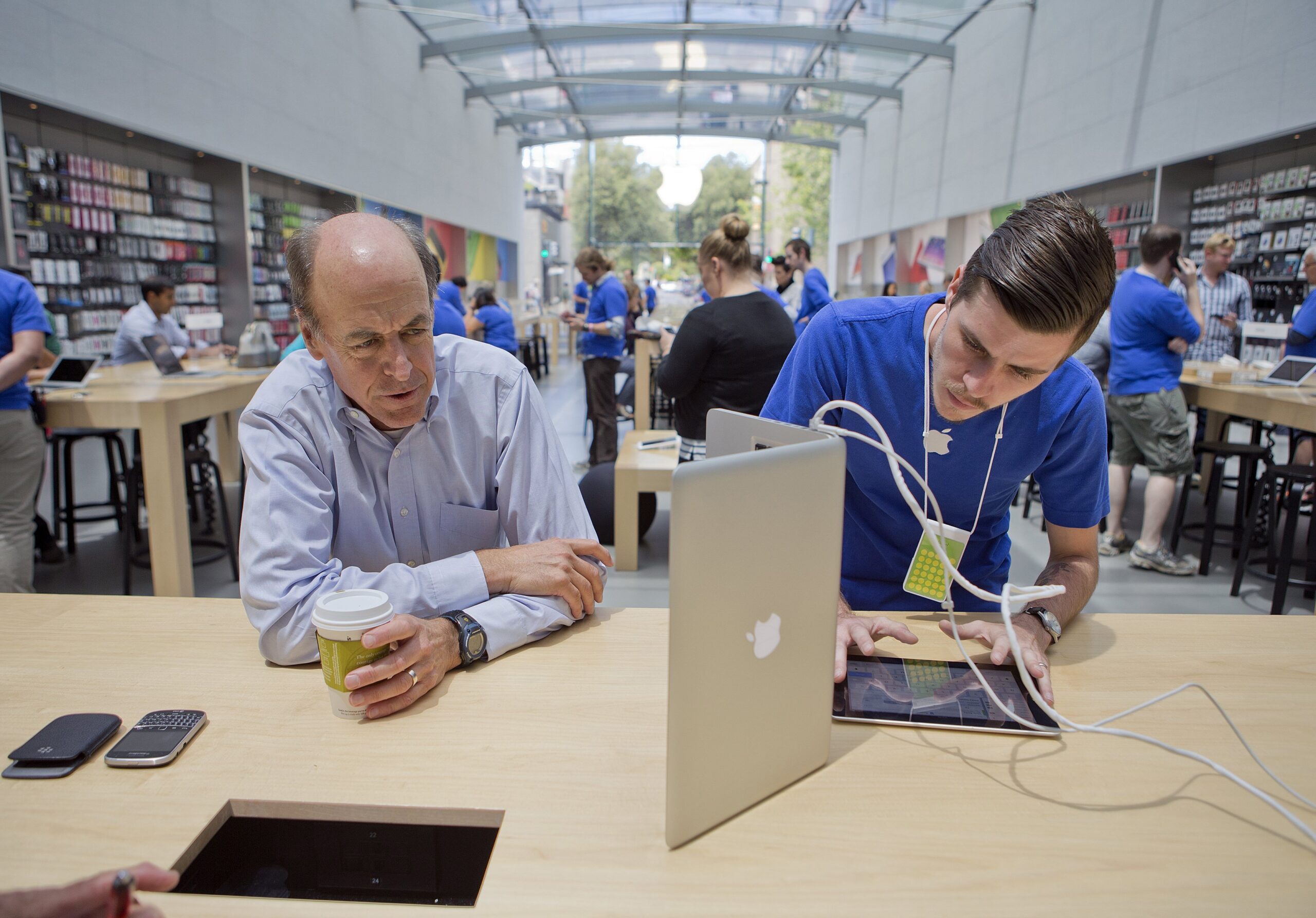 Two men work on a tablet and a laptop in an Apple store.
