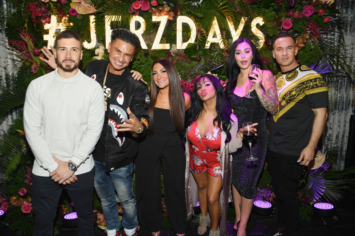 Six people from the cast of "Jersey Shore: Family Vacation" pose in front of a lit-up sign that says, "#JERZDAYS."