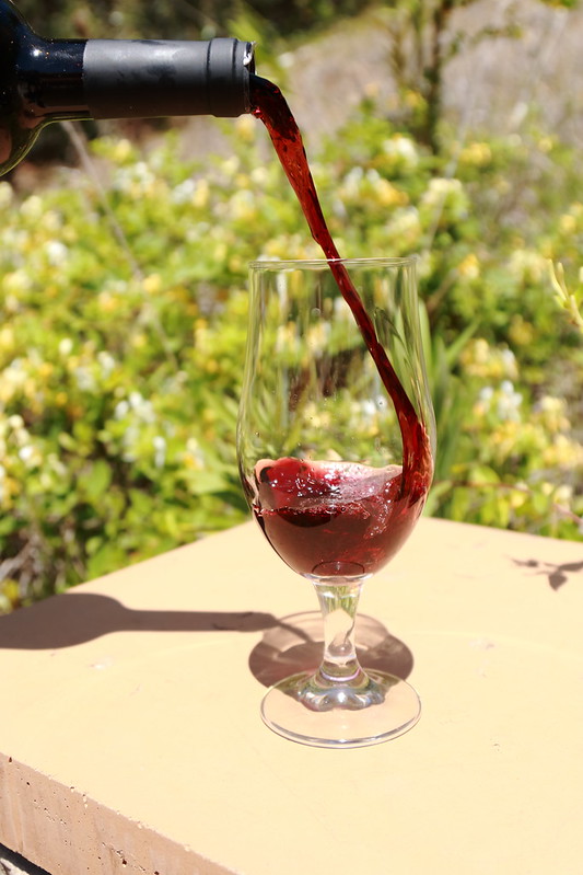 Red wine is poured into a wine glass outdoors on a sunny day.