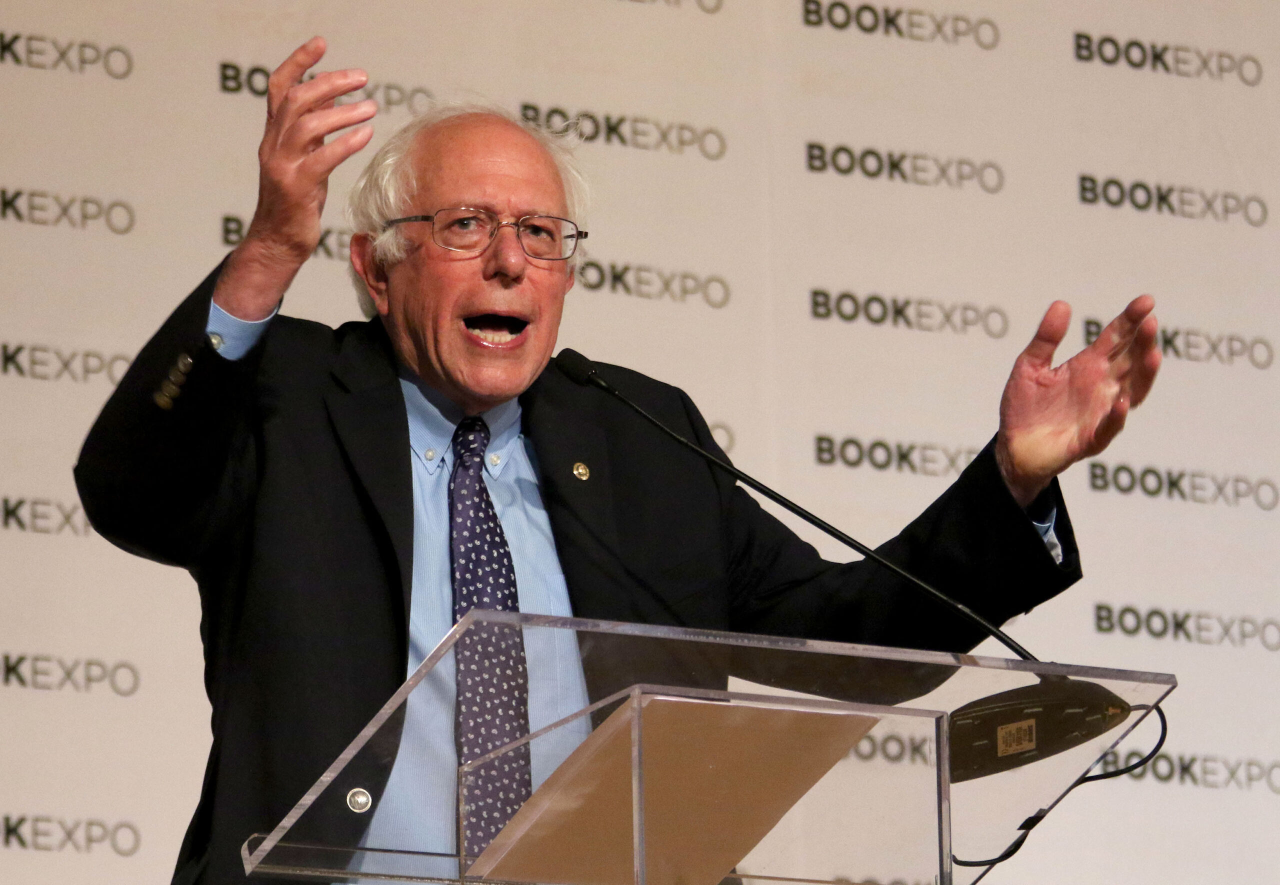 Bernie Sanders speaks with his hands raised by a lectern.