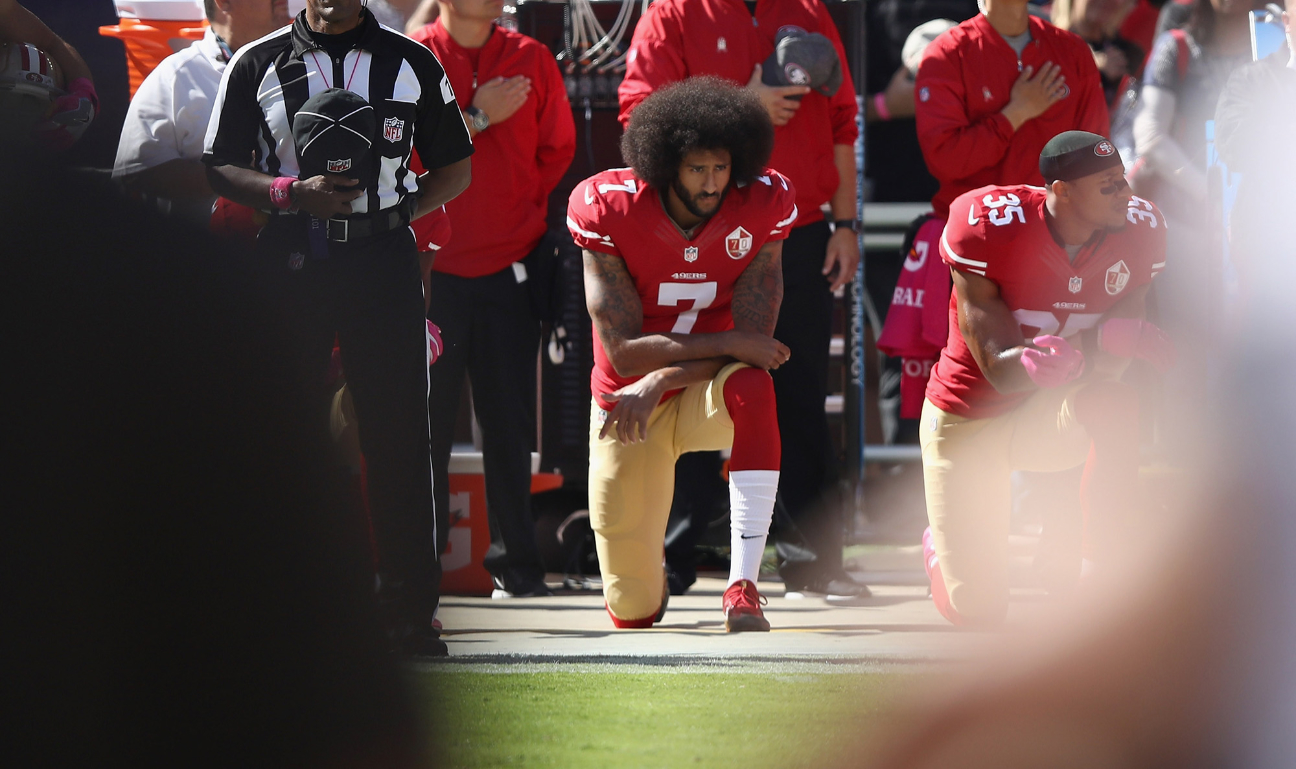 Colin Kaepernick (7) kneels on a football field with several other players during the National Anthem.