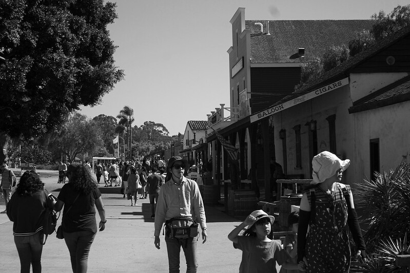 People walk along a walkway near a saloon and several buildings in Old Town San Diego.