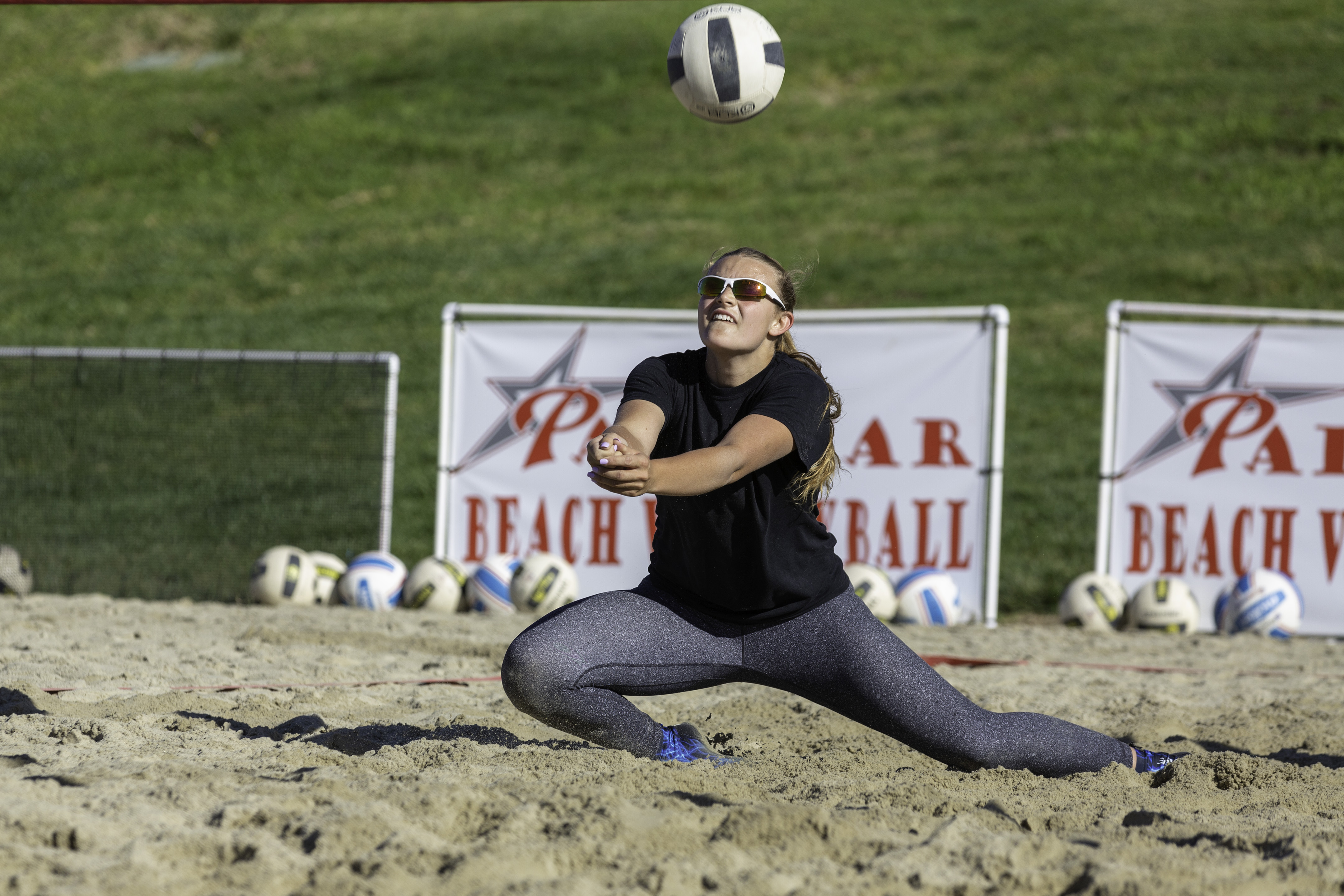 A female Palomar beach volleyball player lunges down to the left as she tries to bump a volleyball with her forearms.