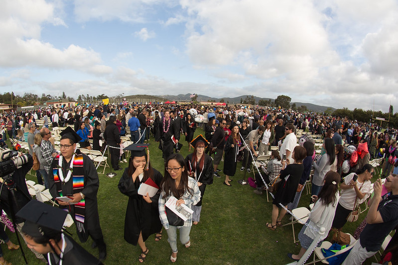 A group of students mingle after a graduating ceremony in an open field.