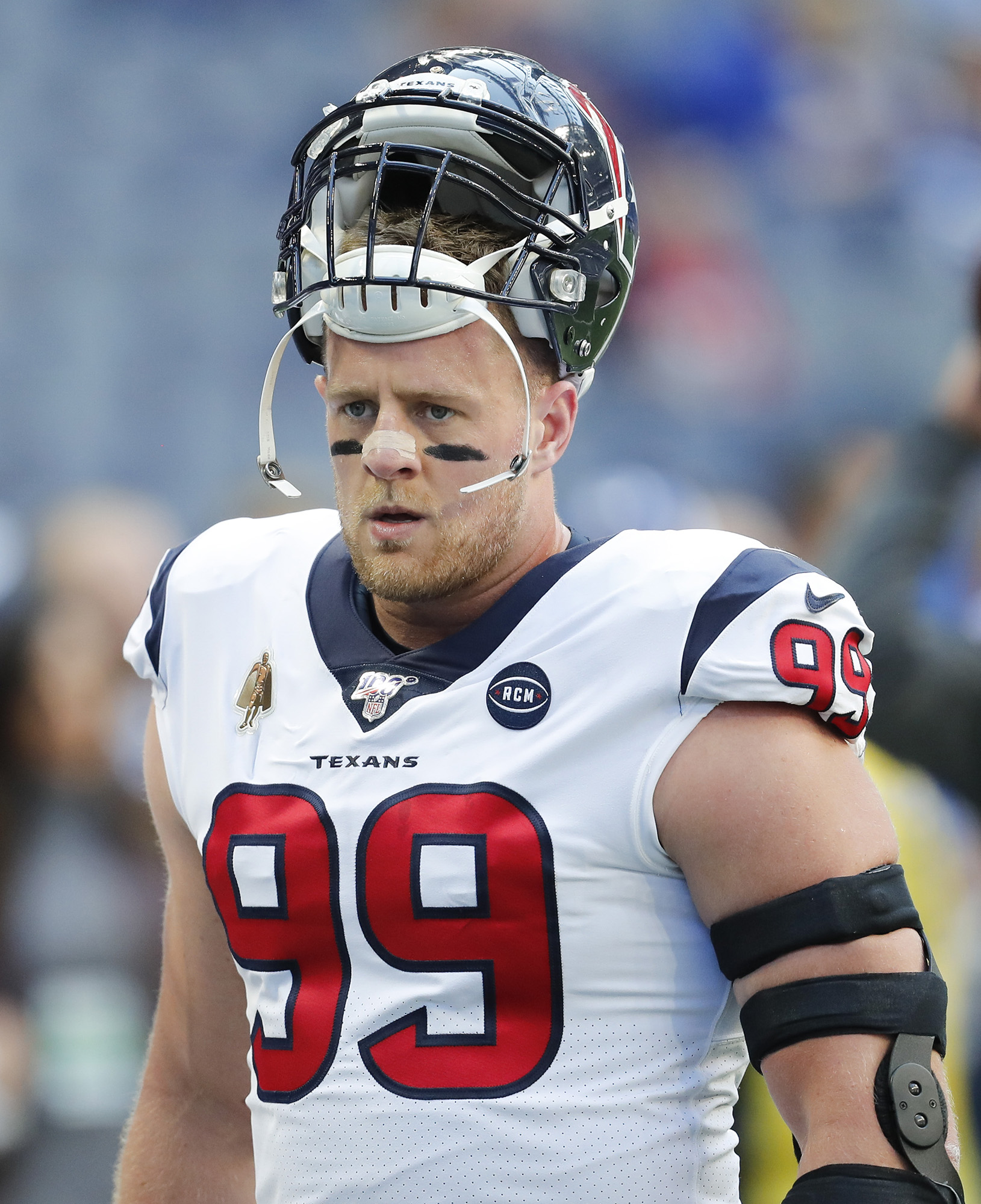 A football player wears a white jersey with the number 99 and the word "Texans" in front of it. He wears his helmt on top of his head, exposing his face.