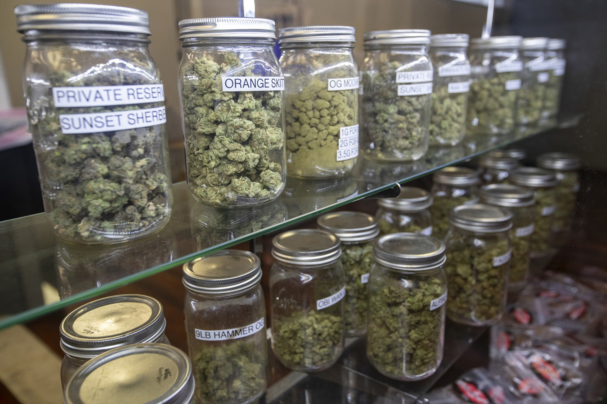 Many dispensary marijuana in jar sit on shelves in a store.