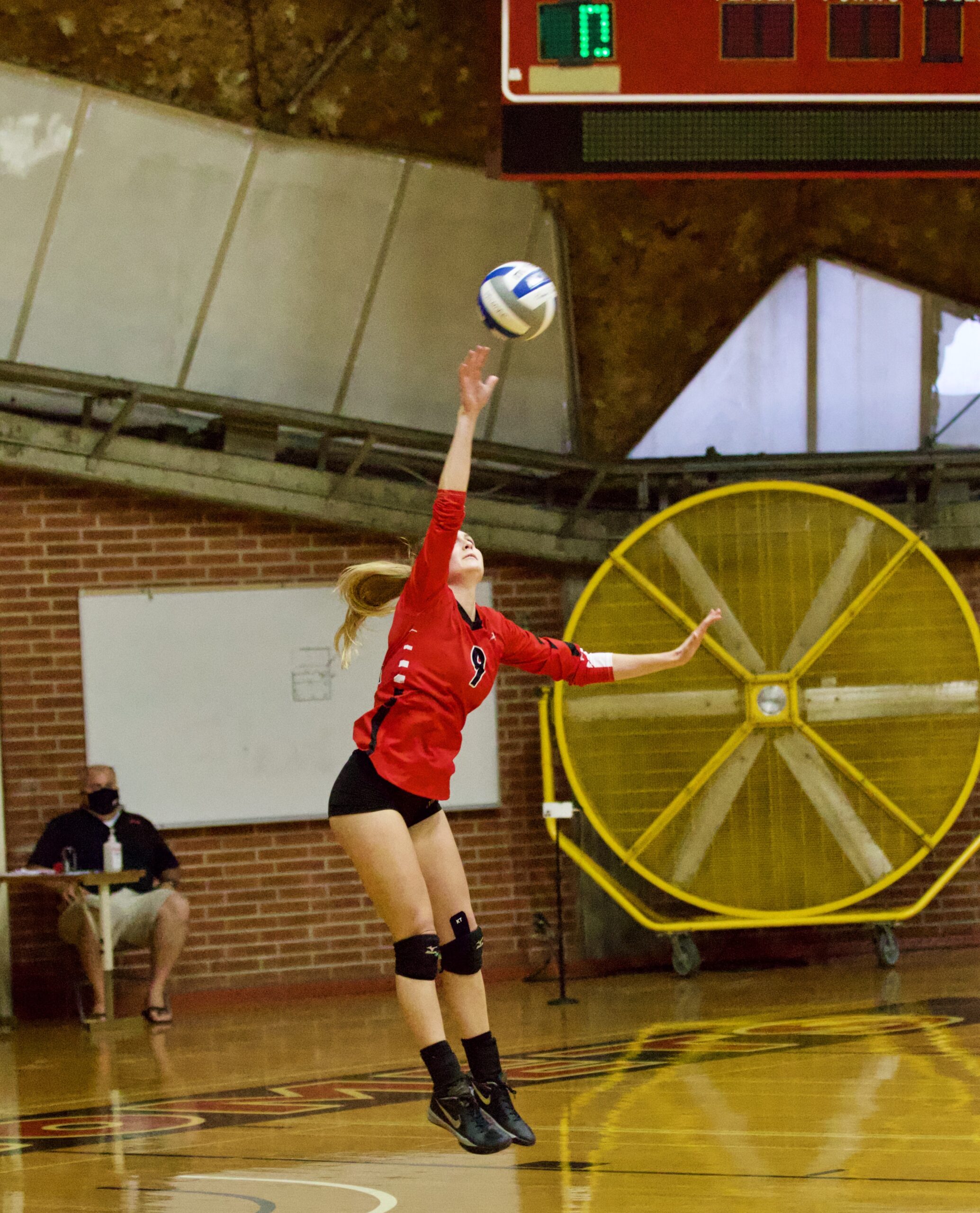 A female Palomar volleyball player leaps up and serves a volleyball with her right hand.