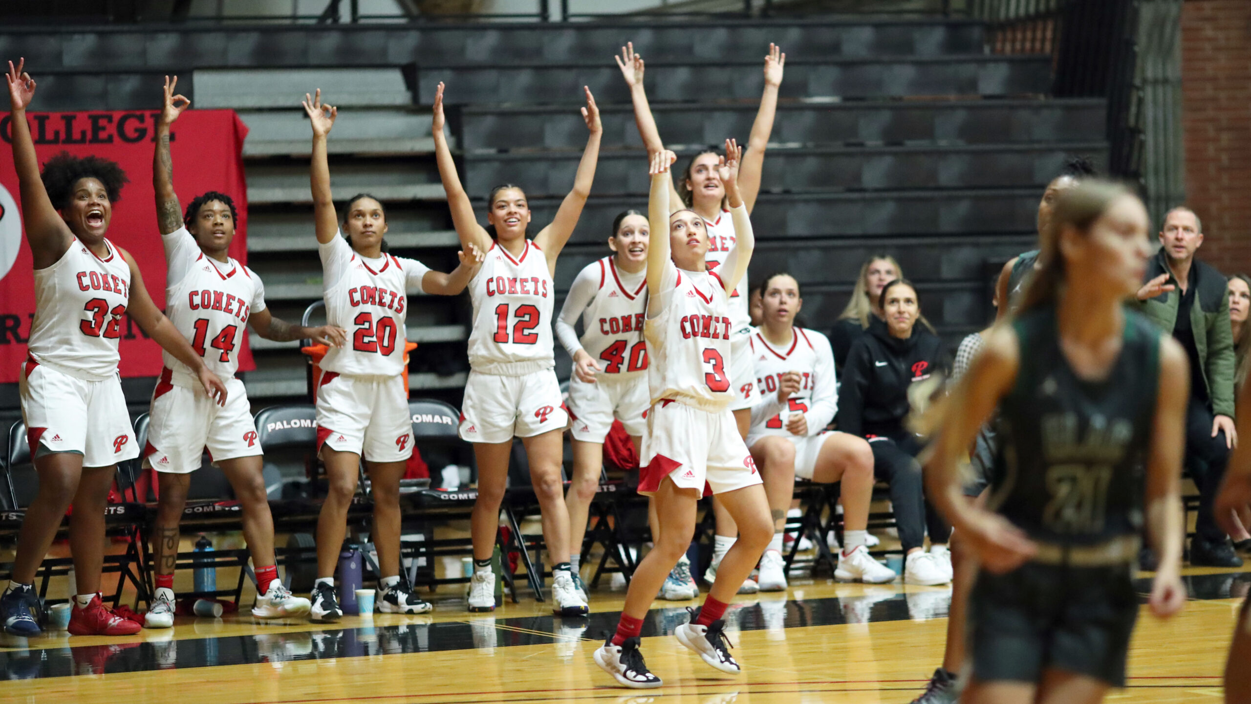 A group of female Palomar basketball players raise their arms and cheer after their teammate (3) shoots a three-pointer.