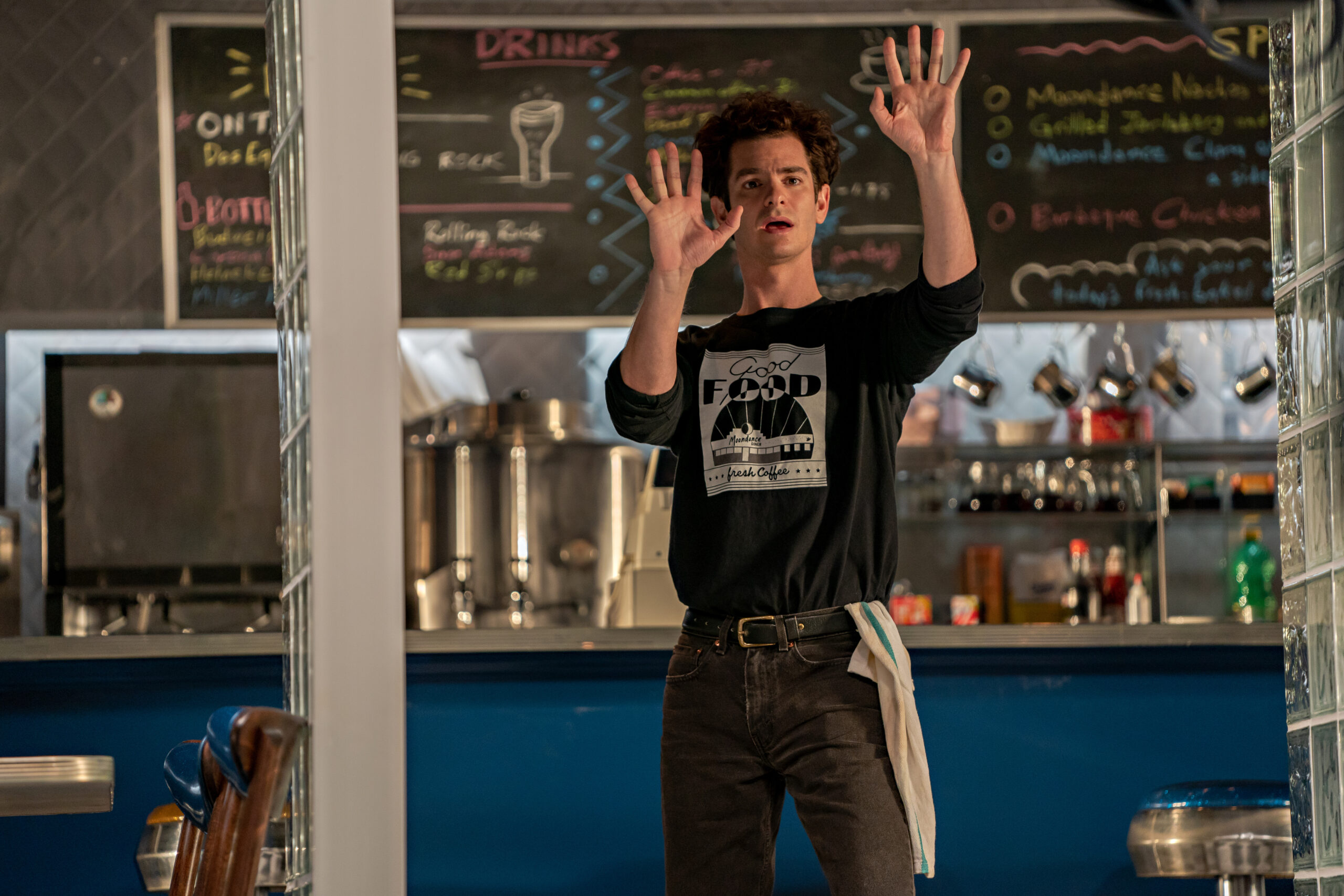 Andrew Garfield as Jonathon Larson in "Tick, Tick...Boom!" holds both hands up as if half-surrendering.