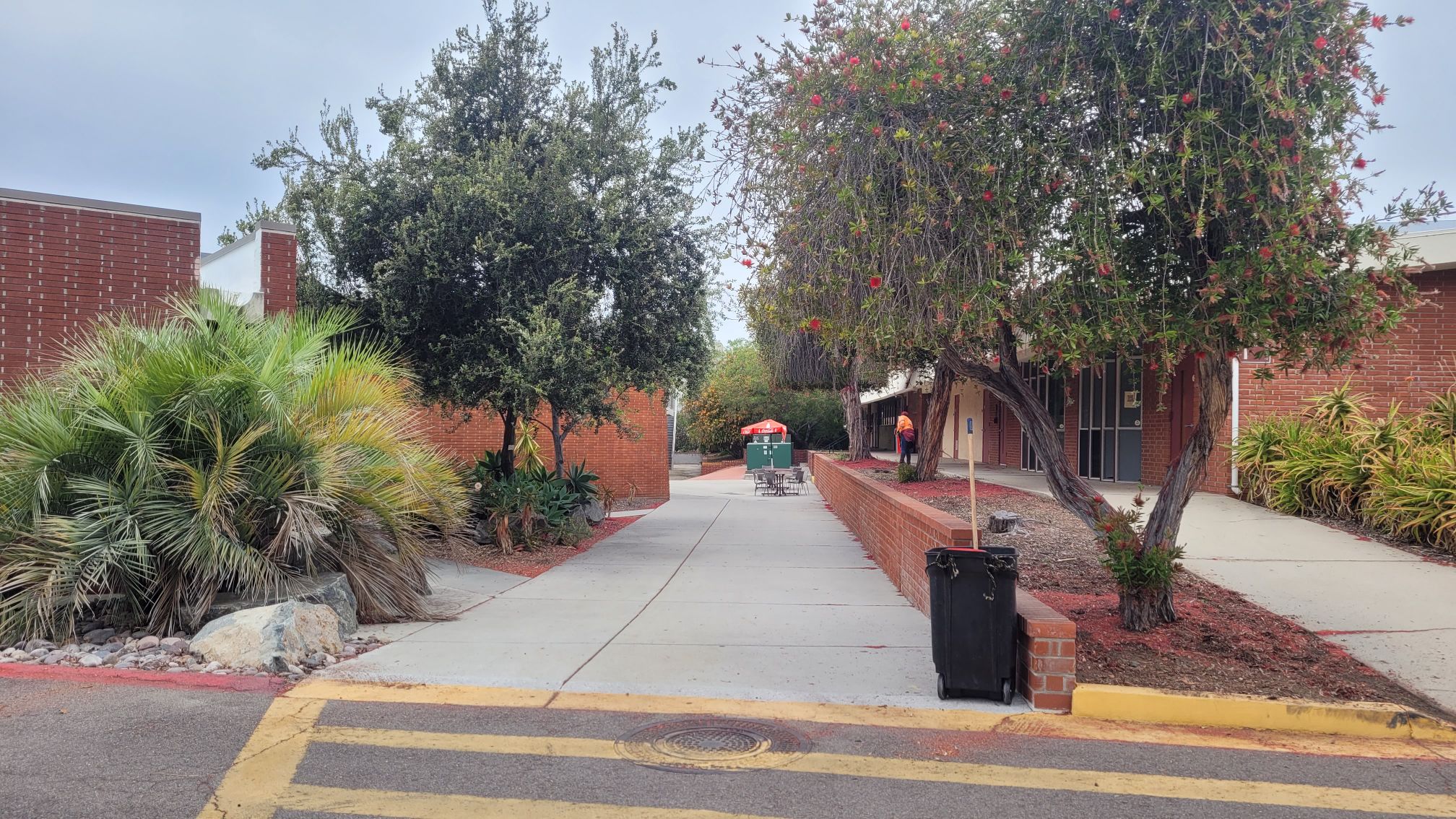 A walkway between two red brick buildings and trees.