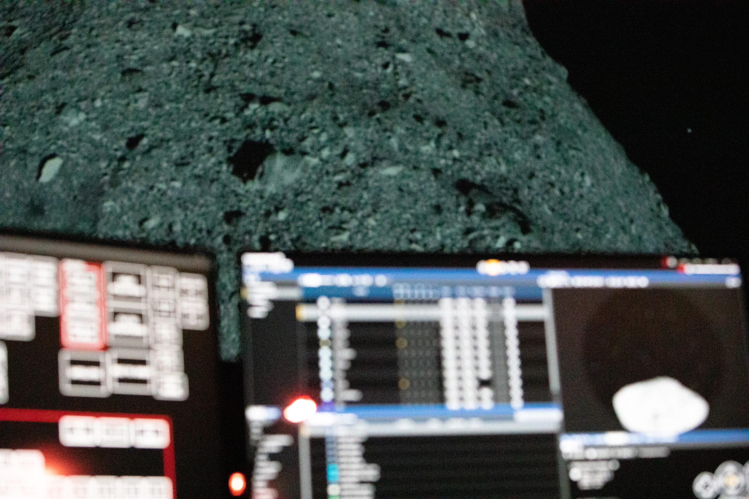Two computer monitors in the foreground (blurred) with an image of the lunar surface in the background.