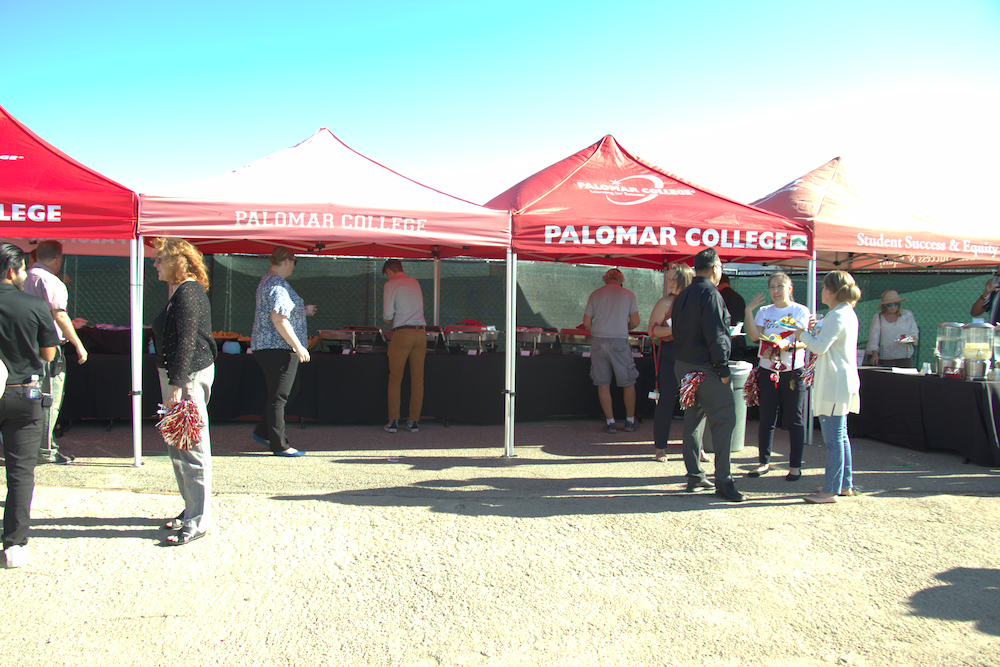 People milling about a row of red tents with "Palomar College" written on it
