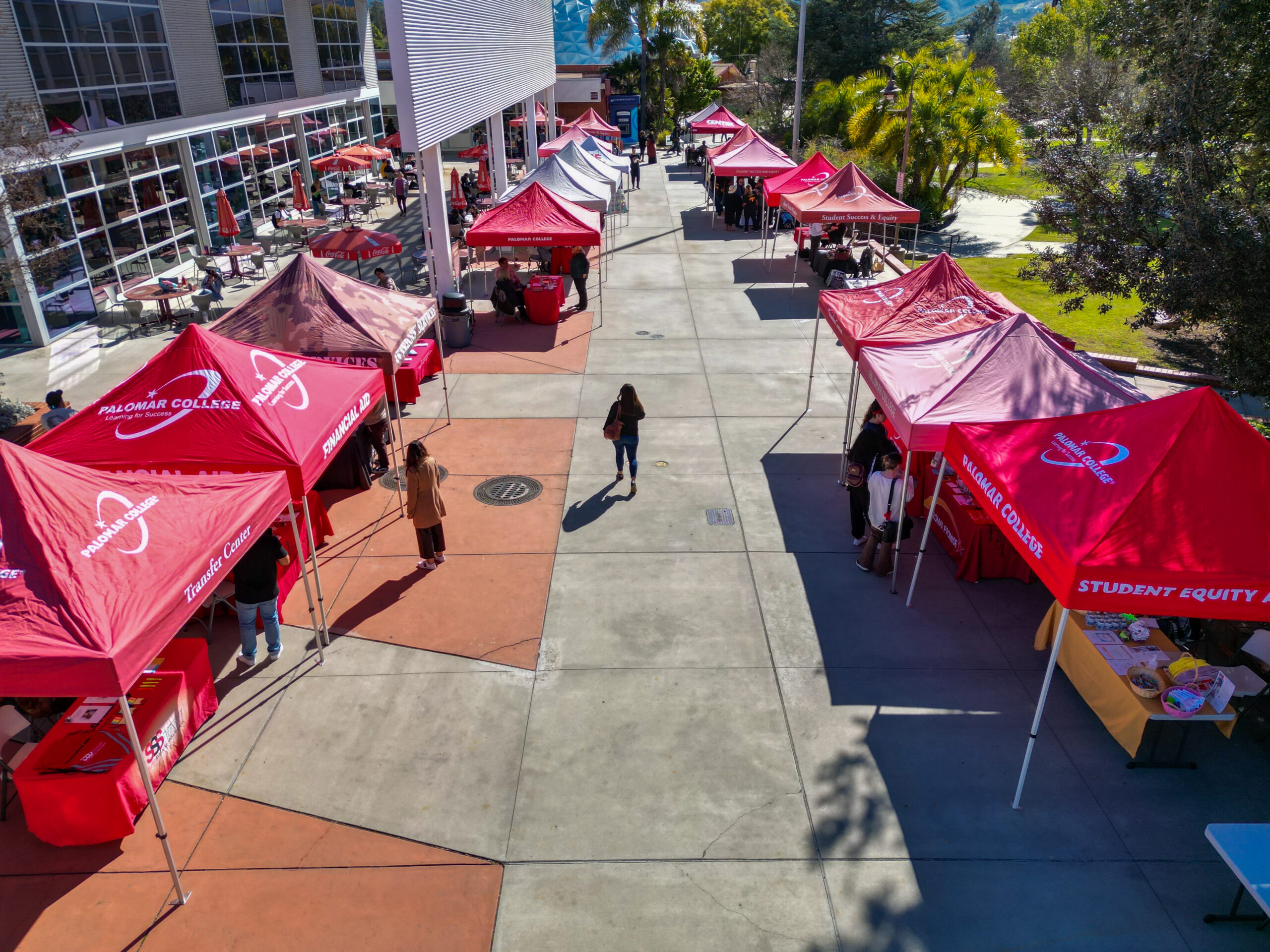 A row of red tents with booths line outside of Palomar College's cafeteria on a sunny day.
