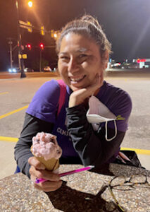 Lisa Burke sits outdoors at night with her left hand resting on her chin and her right hand around an ice-cream cone.