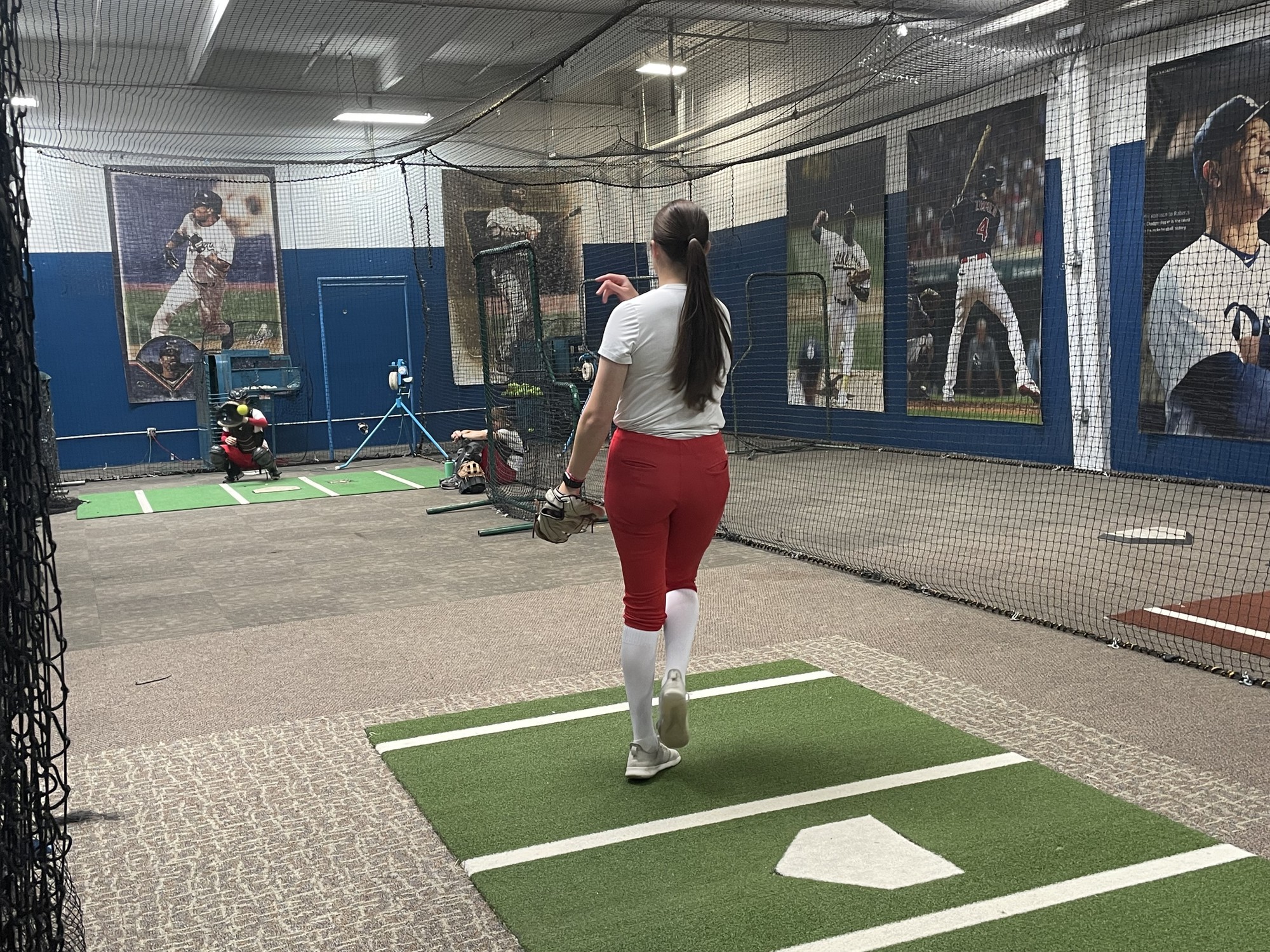 A female softball players practices her pitch inside a training facility.